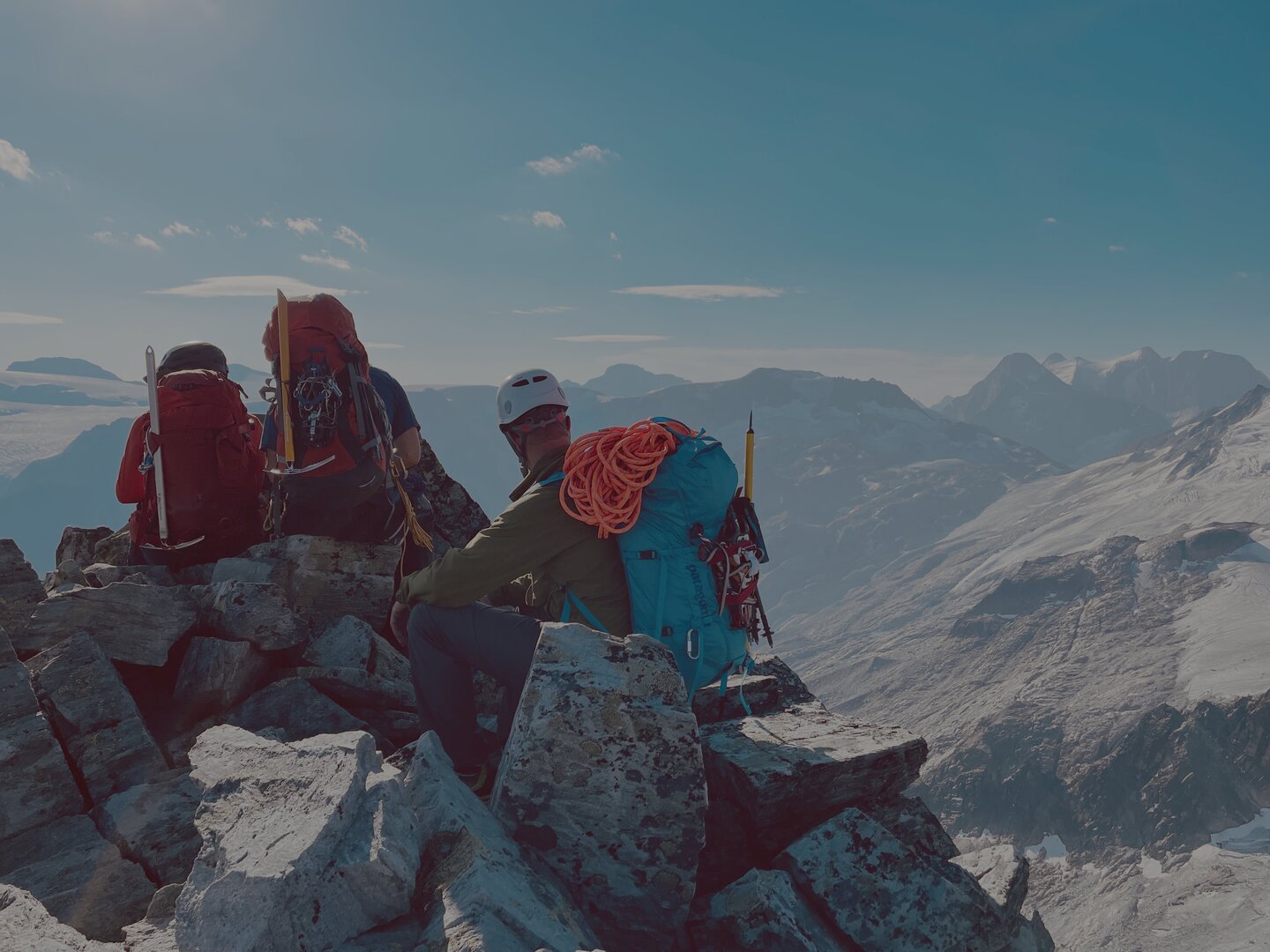 Mountaineers with lightweight packs resting on a rocky summit overlooking snow-covered peaks